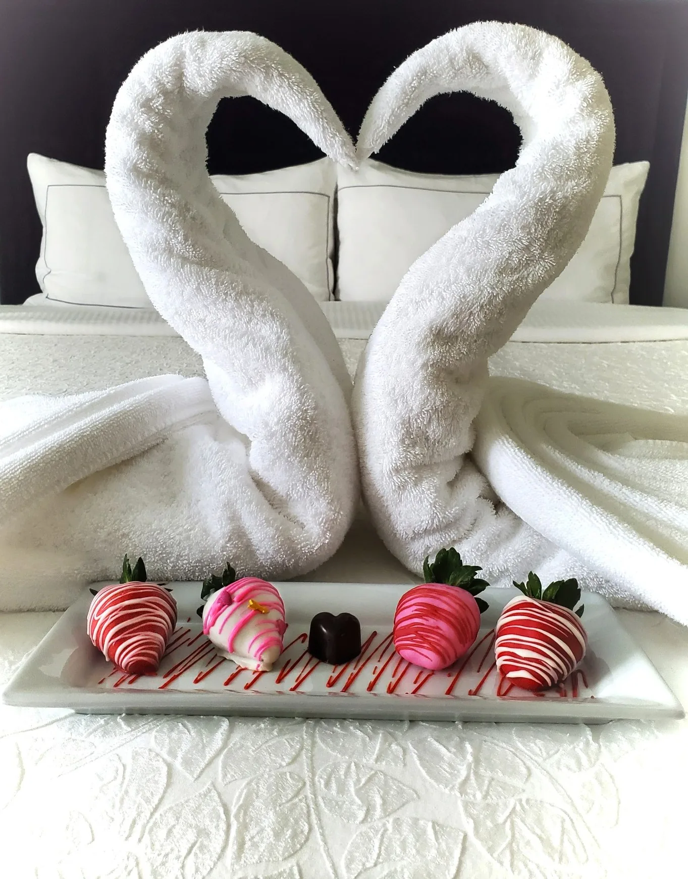 Towel swans and chocolate-covered strawberries prepared on a guest bed